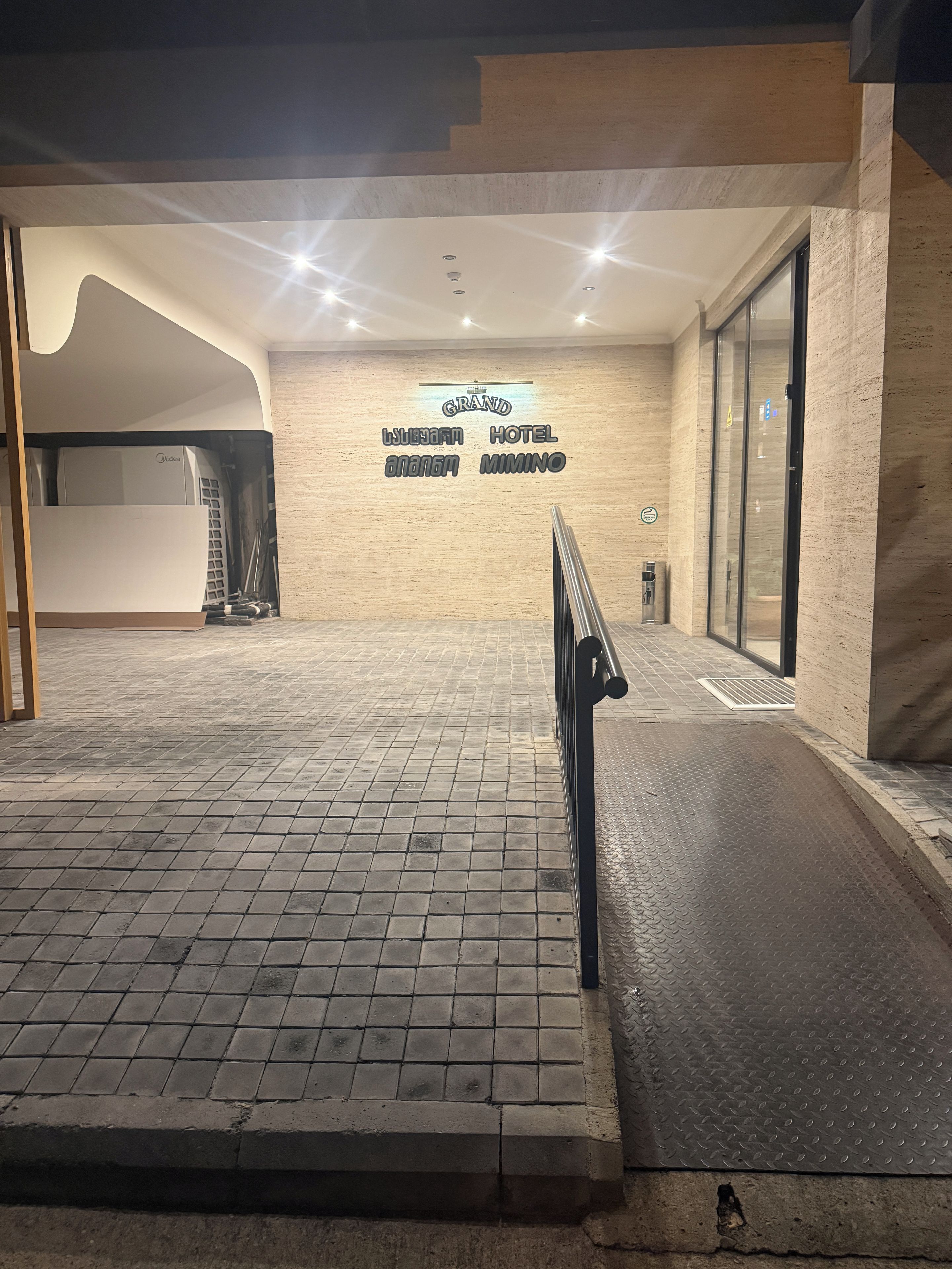 Entrada d'hotel amb un sòl de rajoles, una barana de metall i un senyal que indica el nom de l'hotel.