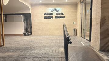 Entrada d'hotel amb un sòl de rajoles, una barana de metall i un senyal que indica el nom de l'hotel.