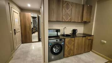 A compact kitchen with a washing machine, wooden cabinets, and a countertop with a coffee maker.