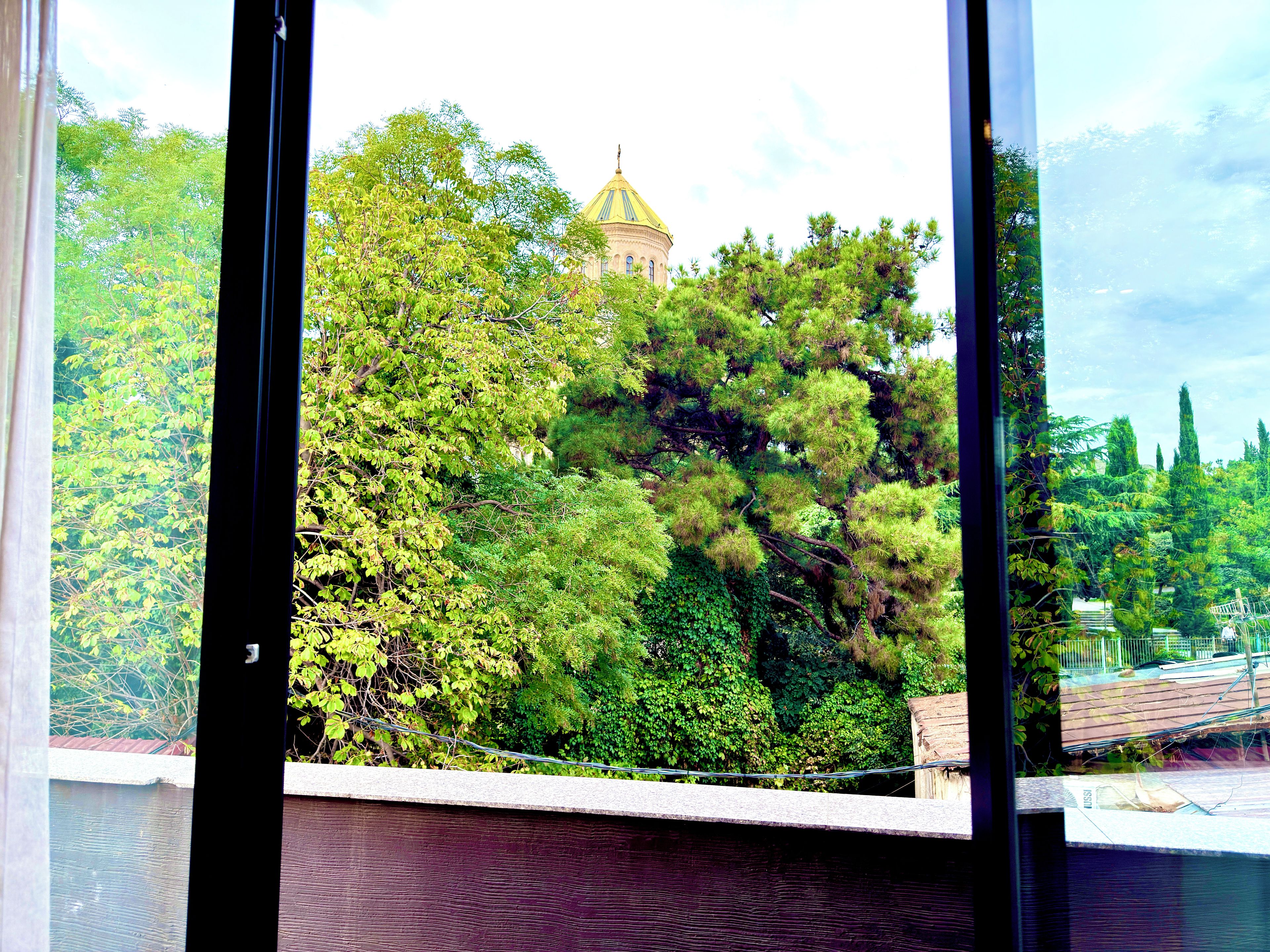 A view through a window with a building featuring a dome structure in the background.