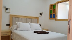 Een keurig opgemaakt bed met een houten hoofdeinde, een nachtkastje en een wandlamp.