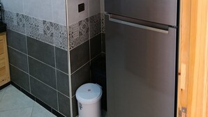 Een keuken met een roestvrijstalen koelkast, houten kastjes en een betegelde vloer.