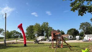 A grassy area with a swing set, a red inflatable structure, and a small green frog toy.