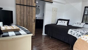 A bedroom with a bed, a TV, a wooden wardrobe, and a small table with items on it.