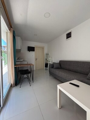 Ein Wohnzimmer mit einer Couch, einem Couchtisch, einem an der Wand befestigten Fernseher und einem Essbereich mit Tisch und Stühlen.
