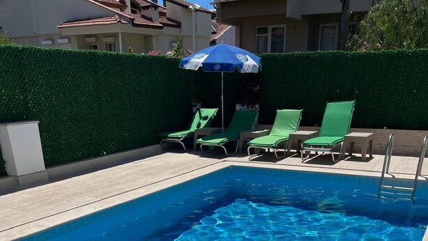 A rectangular swimming pool with clear blue water, surrounded by a low hedge and a tiled deck. - Marmaris apartment with pool (Armutalan)