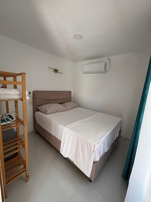 Ein Einzelbett mit Holz-Kopfteil, ein kleines Regal und eine Klimaanlage an der Wand.