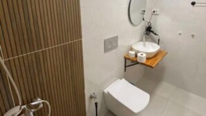 A modern bathroom with a wooden panel wall, a white sink with a mirror, a toilet, and a shower area. - Marmaris apartment with pool (Armutalan)