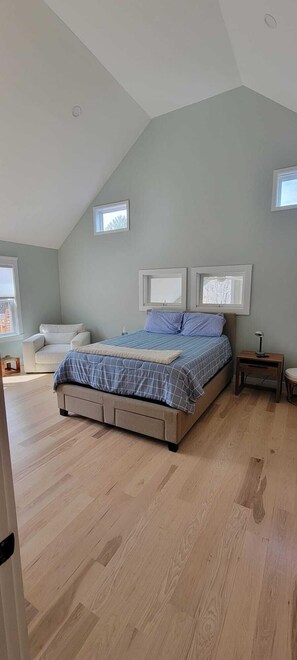 Een slaapkamer met een bed, een stoel, een nachtkastje en een raam.