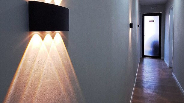 A hallway with a modern wall-mounted light fixture and recessed ceiling lights.
