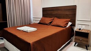 A neatly made bed with a brown bedspread and pillows, a bedside table with a remote control, and a wall-mounted light fixture.
