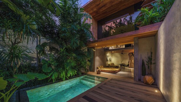 A modern outdoor living area with a wooden deck, a swimming pool, and lush tropical plants.