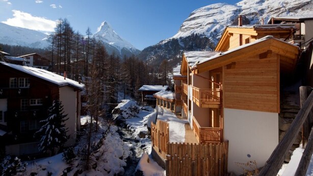 A wooden chalet with a balcony, surrounded by snow-covered trees and mountains in the background. - Matterhorn Gazes, Luxury Embraces 1000 (Valais)