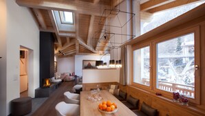 A spacious dining area with a long wooden table, multiple seating options, and a large window offering a view of the outdoors. - Matterhorn Gazes, Luxury Embraces 1000 (Valais)