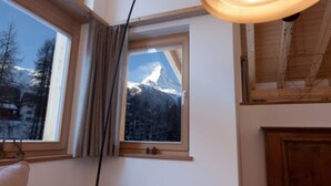 A cozy room with a large window overlooking a snowy mountain, a wooden ceiling, and a black floor lamp. - Matterhorn Gazes, Luxury Embraces 1000 (Valais)