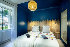 A room with two beds, a wooden headboard, a hanging light fixture, and a window with a view.