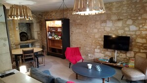 A living room with a stone wall, a fireplace, a television, and a dining area with chairs and a table.