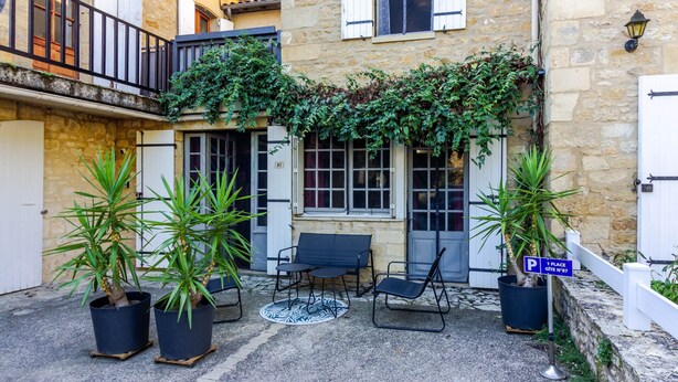 A courtyard with stone walls, a black metal bench, two potted plants, and a sign indicating a parking spot.