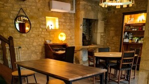 A rustic interior with a wooden table and stools, stone walls, and a hanging light fixture.