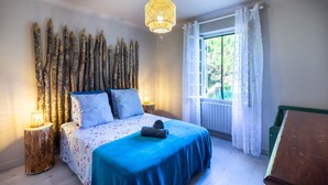 A bedroom with a bed, bedside lamps, a window with curtains, and a hanging light fixture.