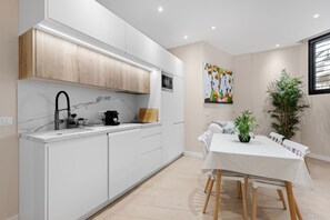 A modern kitchen with white cabinetry, a marble backsplash, and a dining area with a table and chairs.
