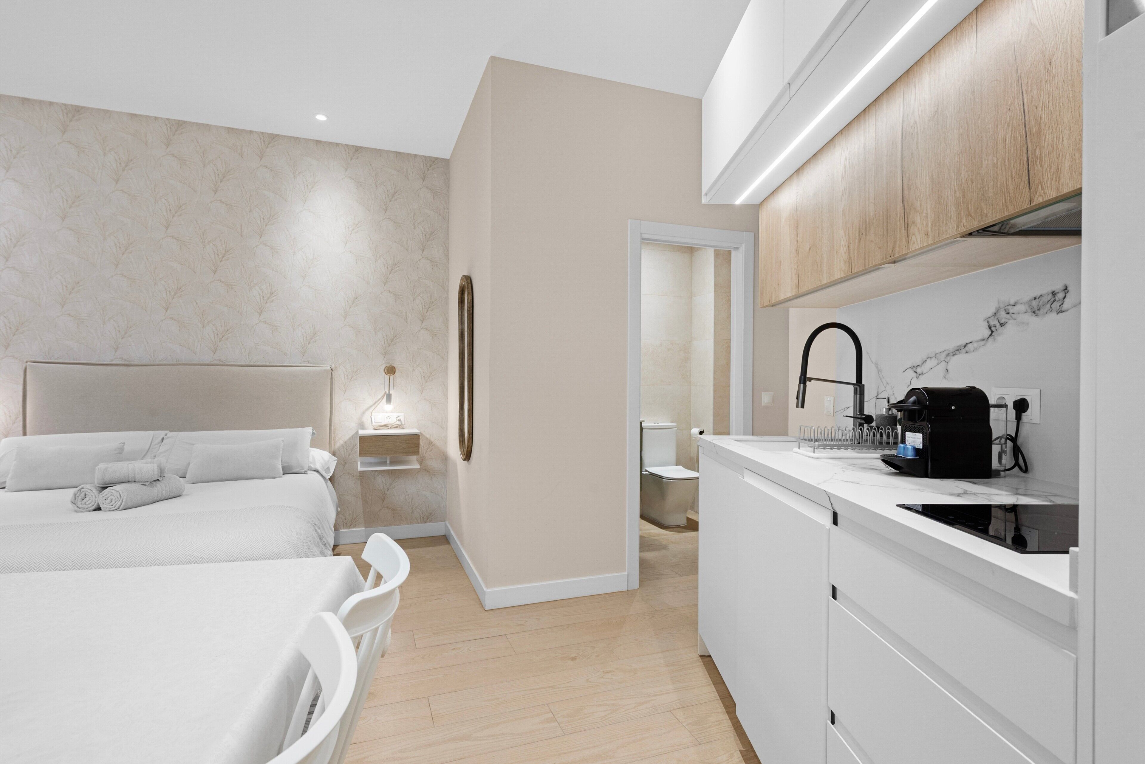 Una habitación de hotel moderna con cama, mesita de noche y una zona de kitchenette.
