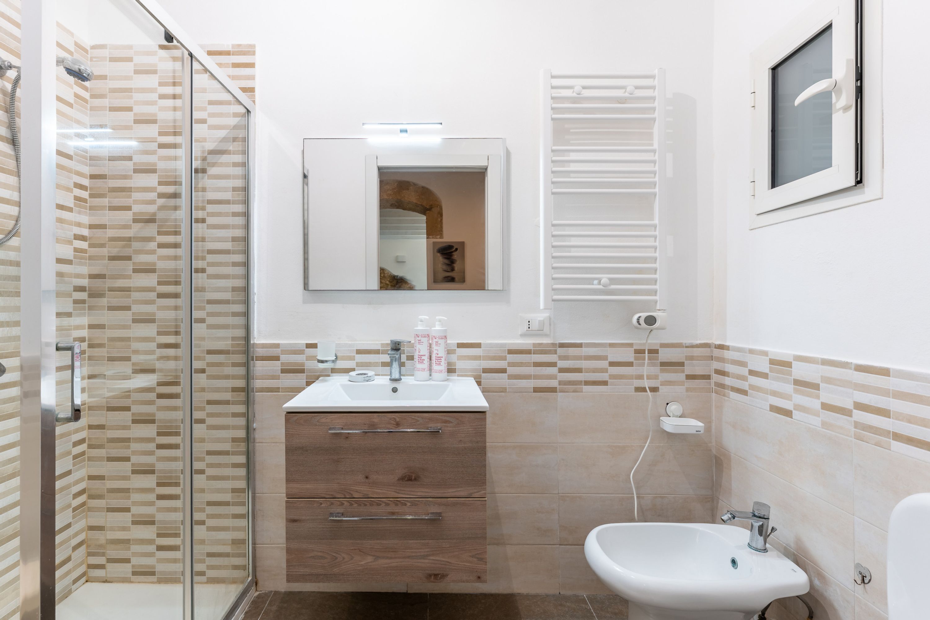 Ein Badezimmer mit Duschkabine aus Glas, einem weißen Waschbecken mit Spiegel darüber und einem weißen Bidet.