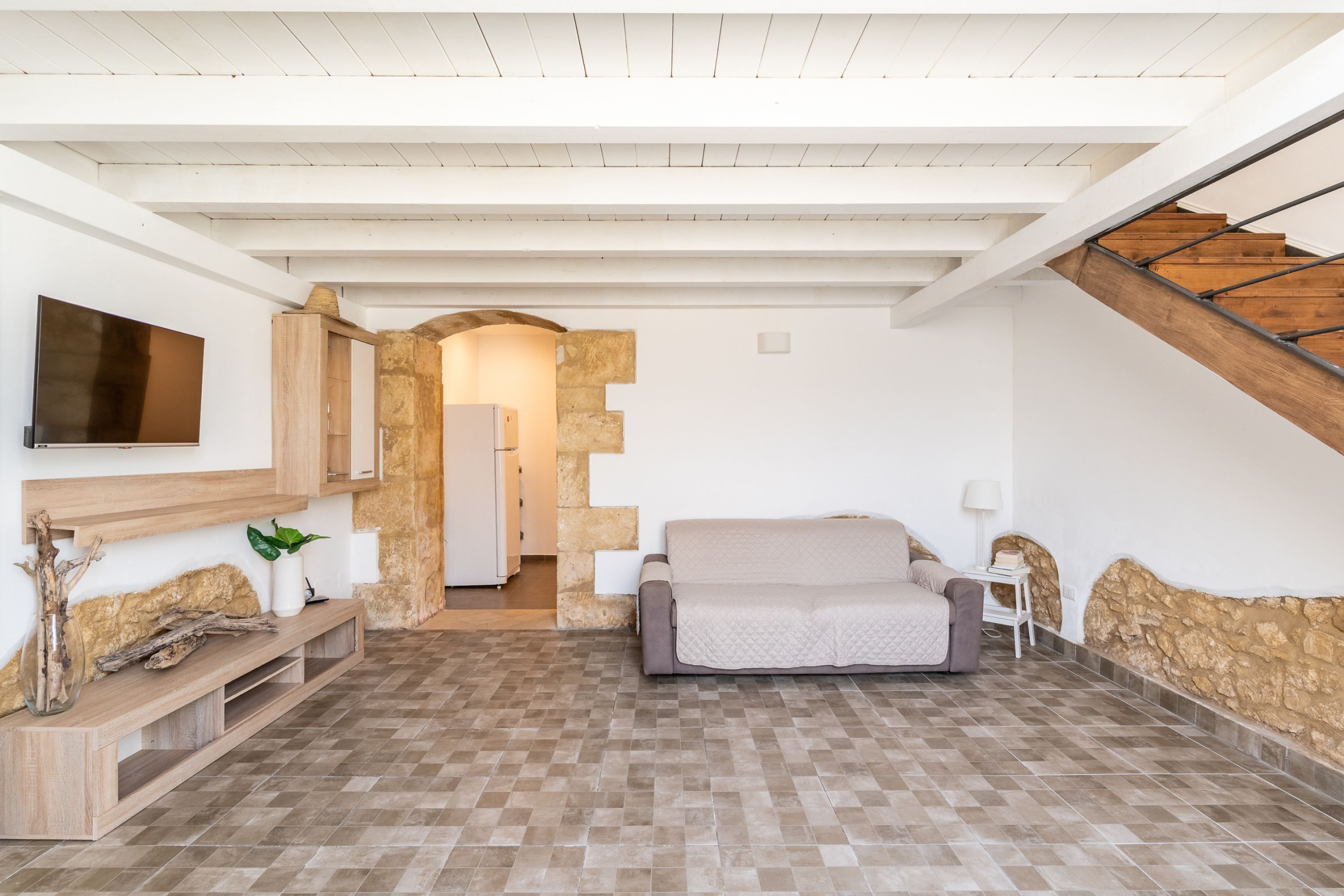 A spacious living area with a wooden bench, a sofa, and a TV mounted on the wall.