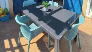 Une terrasse extérieure avec une table et des chaises, des volets bleus et un pot de fleurs.