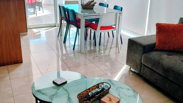 Ein modernes Wohnzimmer mit Glastisch, einer Couch und einem Essbereich mit Stühlen.