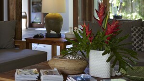 A wooden-framed room with a sofa, a coffee table with magazines, a lamp, and a potted plant.