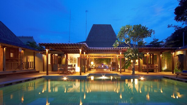 A poolside area with a covered seating area, a pool, and a building with a sloped roof.