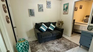 Uma sala de estar com um sofá cinza escuro, duas almofadas listradas, um tapete estampado e um vaso verde.