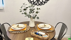 Une table de salle à manger ronde, accompagnée de quatre chaises, un vase rempli de feuillage vert et un élément décoratif mural.