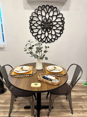 A round dining table with four chairs, a vase with green foliage, and a decorative wall piece.
