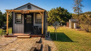 Une cabane avec une véranda, une pancarte indiquant « CABANE », et un moulin à vent en arrière-plan.