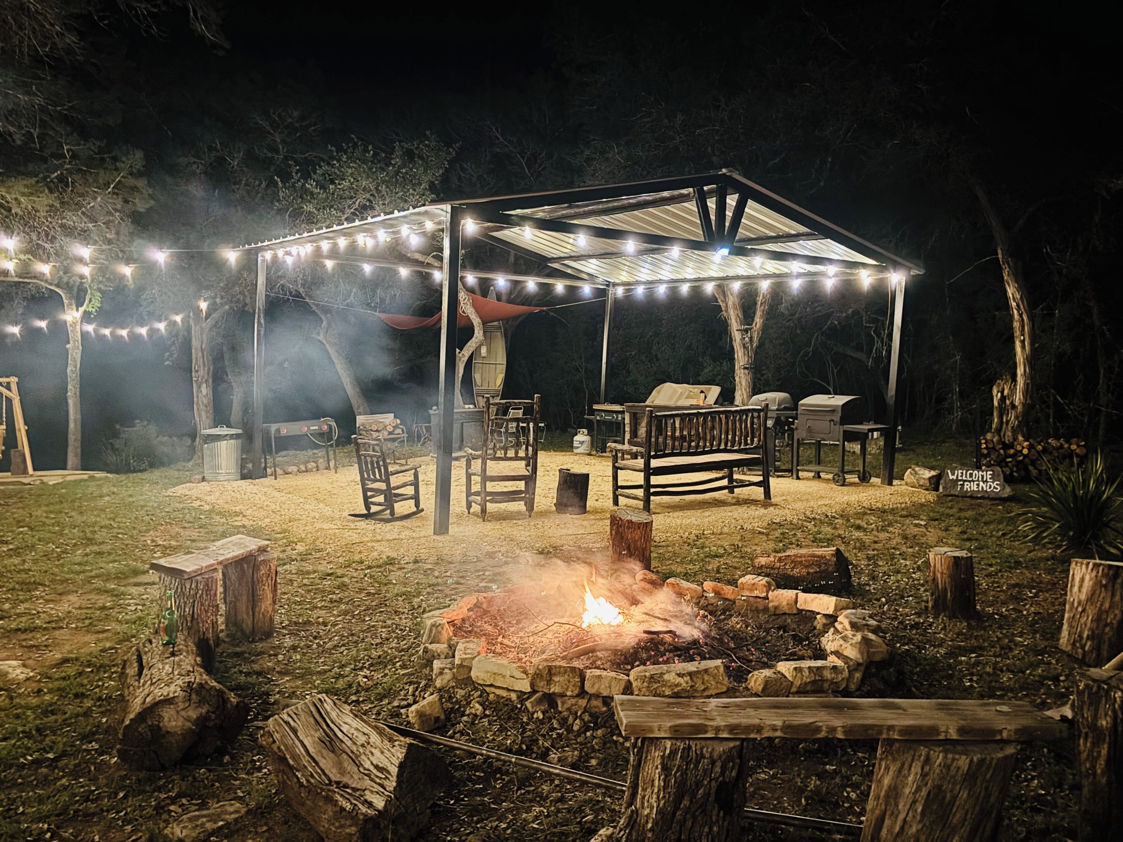 An outdoor patio area with a fire pit, wooden furniture, and string lights.