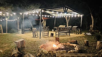 An outdoor patio area with a fire pit, wooden furniture, and string lights.