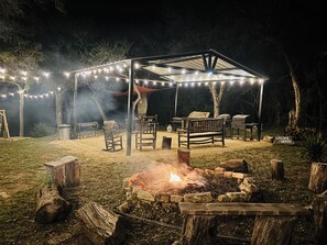 An outdoor patio area with a fire pit, wooden furniture, and string lights.