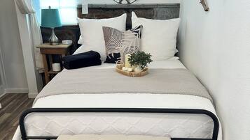 A neatly arranged bedroom with a bed, bedside table, lamp, and a small bench.