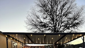 Un espace extérieur abrité avec un sol en gravier, une construction en bois dotée d’une fenêtre et un arbre en arrière-plan.