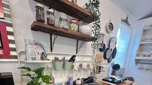 Une cuisine compacte dotée d’un lave-vaisselle encastré, d’un évier et d’un plan de travail en bois. Des étagères au-dessus du plan de travail servent à ranger des bocaux et des ustensiles de cuisine.