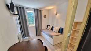 A compact room with a wooden dining table, a built-in bench with cushions, a radiator, and a window with curtains.