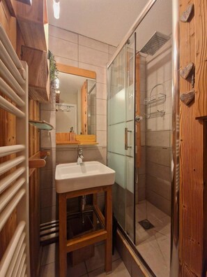 A bathroom with a wooden vanity, a sink, a glass shower enclosure, and a mirror.