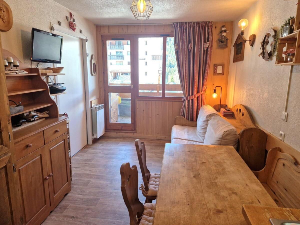 Een gezellige kamer met een houten eettafel, een bank, een televisie en een raam met gordijnen.
