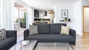 Ein modernes Wohnzimmer mit einem grauen Sofa, einem Glastisch und Blick in den Küchenbereich.