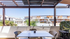 Eine Terrasse im Freien mit Tisch und Stühlen, einer Pergola und Blick auf Wohnhäuser.