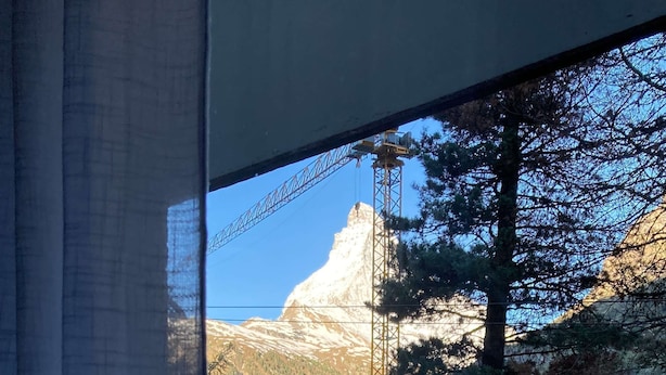A window view of a mountain with a bridge, trees, and buildings.