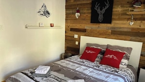 A bed with patterned bedding, two red pillows, a wooden headboard, and a wall with a mountain decal.