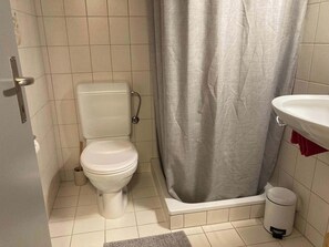 A bathroom with a toilet, shower curtain, sink, and trash can. - Chalet Studio Zermatt: Matterhorn Views & Terrace (Zermatt)